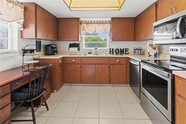 kitchen with light countertops, light tile patterned floors, brown cabinetry, stainless steel appliances, and a sink