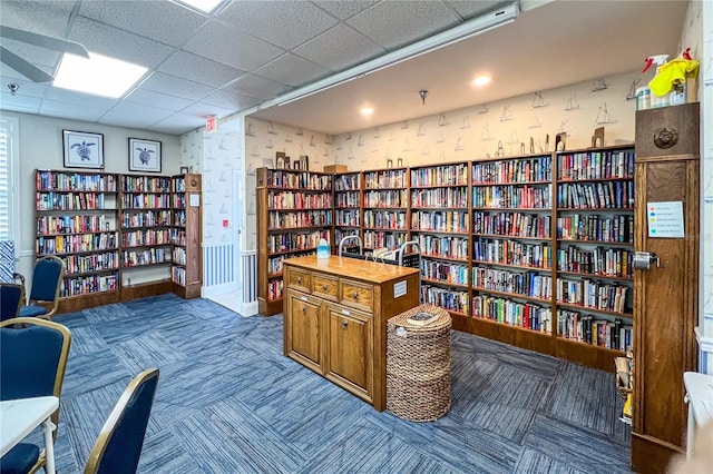 living area featuring wallpapered walls, carpet flooring, wall of books, and a paneled ceiling