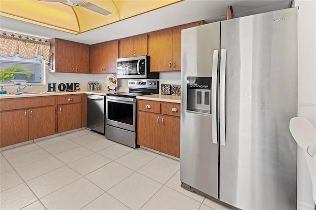 kitchen featuring light tile patterned floors, a sink, stainless steel appliances, light countertops, and brown cabinets