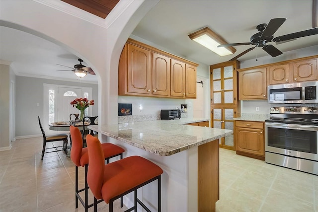 kitchen with appliances with stainless steel finishes, a kitchen bar, kitchen peninsula, and ceiling fan