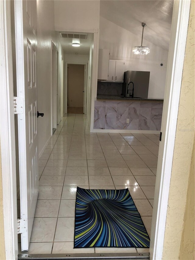 hallway with lofted ceiling, an inviting chandelier, and light tile patterned flooring