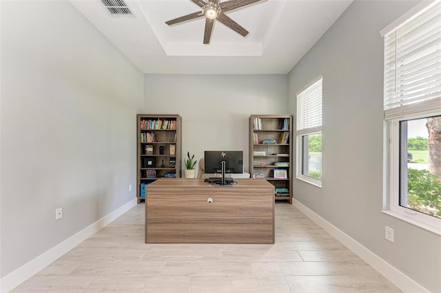 unfurnished office featuring a raised ceiling, plenty of natural light, ceiling fan, and light hardwood / wood-style floors