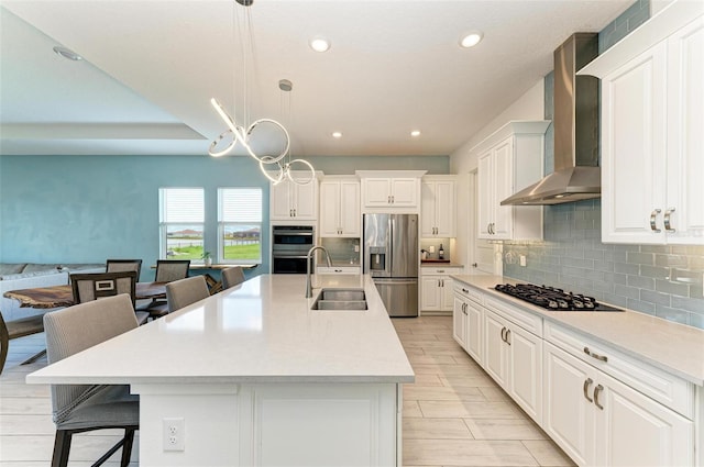 kitchen featuring sink, hanging light fixtures, appliances with stainless steel finishes, a breakfast bar, and wall chimney range hood