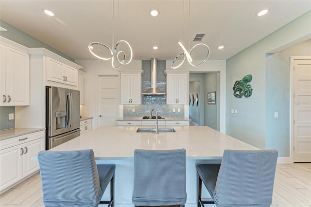 kitchen featuring light hardwood / wood-style flooring, decorative light fixtures, wall chimney exhaust hood, and stainless steel refrigerator with ice dispenser