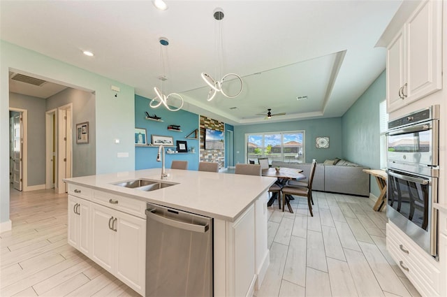 kitchen with a kitchen island with sink, white cabinetry, stainless steel appliances, sink, and hanging light fixtures