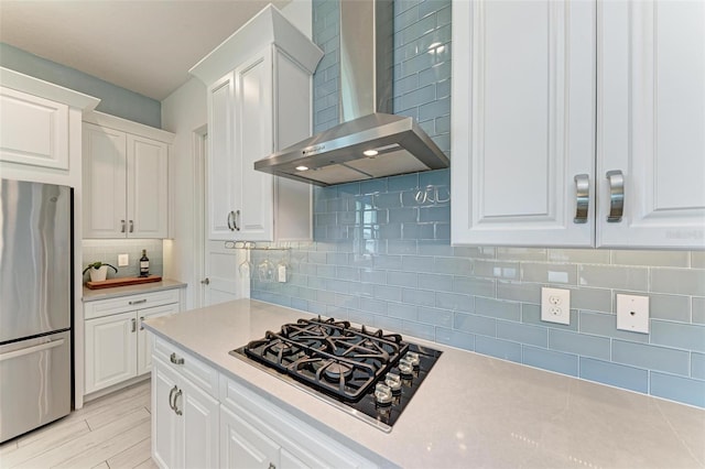 kitchen with stainless steel fridge, tasteful backsplash, wall chimney exhaust hood, black gas cooktop, and white cabinets