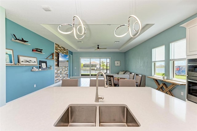 kitchen with white cabinets, ceiling fan with notable chandelier, a raised ceiling, and sink