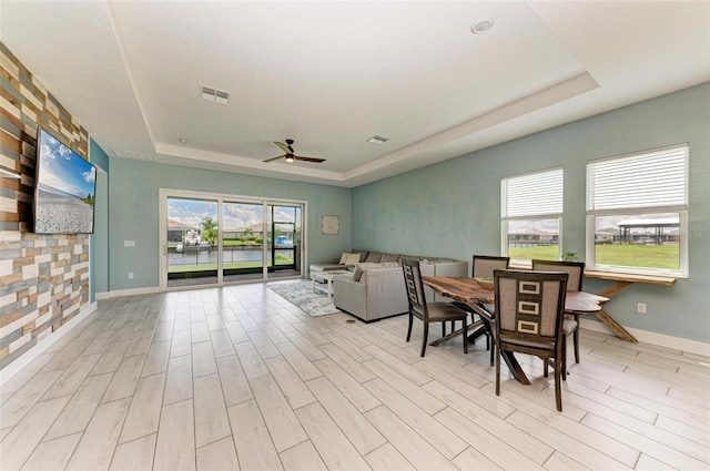 dining area featuring light hardwood / wood-style flooring, ceiling fan, and a tray ceiling