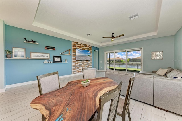 dining room featuring a tray ceiling, ceiling fan, light hardwood / wood-style floors, and a textured ceiling