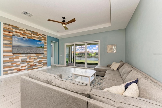 living room with light wood-type flooring, a textured ceiling, a tray ceiling, and ceiling fan