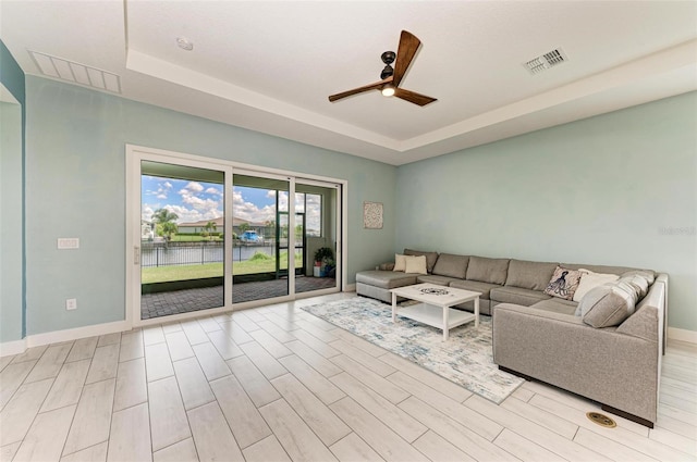 unfurnished living room with a tray ceiling, light wood-type flooring, and ceiling fan