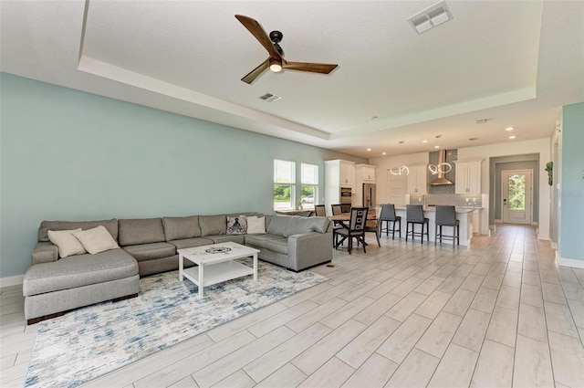 living room with a tray ceiling, light hardwood / wood-style flooring, and ceiling fan