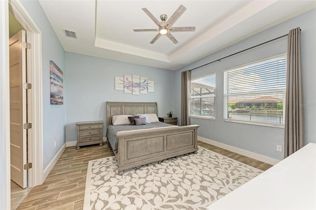 bedroom featuring a raised ceiling, ceiling fan, and light wood-type flooring