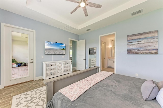 bedroom with a tray ceiling, ceiling fan, connected bathroom, and light hardwood / wood-style flooring