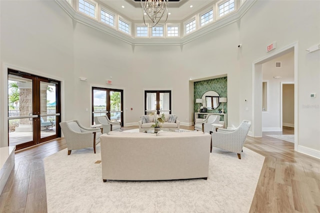 living room featuring a chandelier, a high ceiling, light wood-type flooring, and french doors