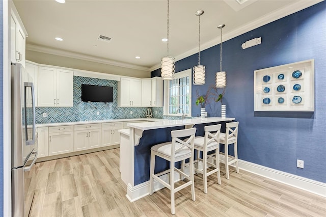 kitchen with light wood-type flooring, pendant lighting, a kitchen bar, and stainless steel refrigerator