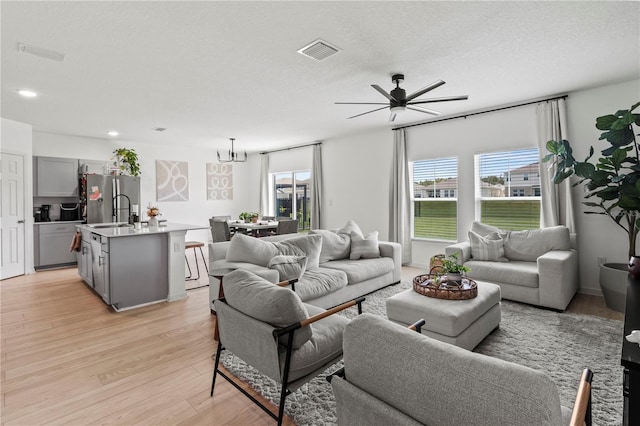 living room featuring a textured ceiling, sink, ceiling fan with notable chandelier, and light wood-type flooring