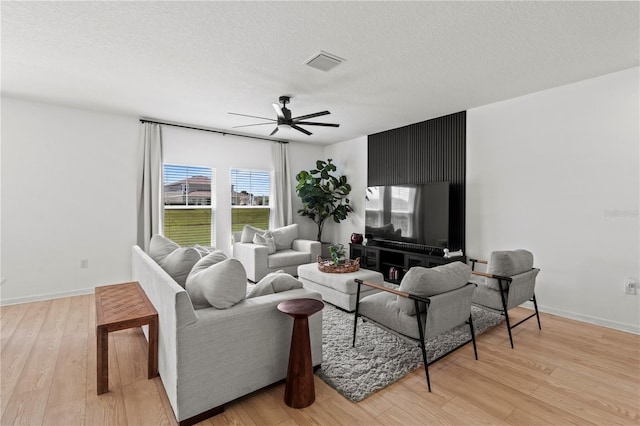 living room with a textured ceiling, ceiling fan, and light hardwood / wood-style floors