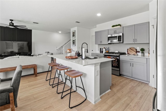 kitchen featuring light wood-type flooring, stainless steel appliances, sink, ceiling fan, and a center island with sink