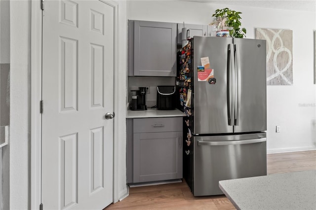 kitchen featuring light wood-type flooring, light stone counters, stainless steel refrigerator, and gray cabinetry