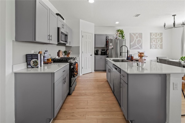 kitchen featuring gray cabinetry, appliances with stainless steel finishes, light hardwood / wood-style floors, sink, and a kitchen island with sink