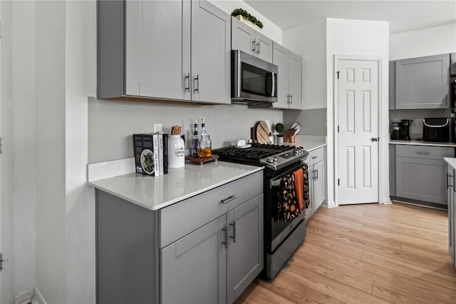 kitchen with gray cabinetry, light wood-type flooring, and gas stove