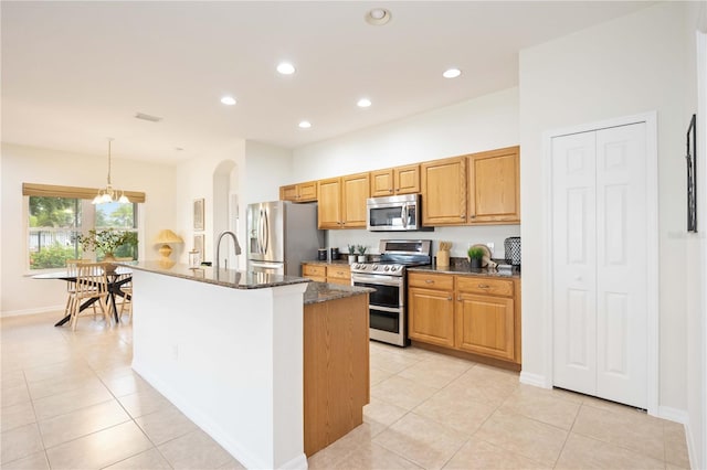 kitchen with appliances with stainless steel finishes, recessed lighting, dark stone counters, and an island with sink