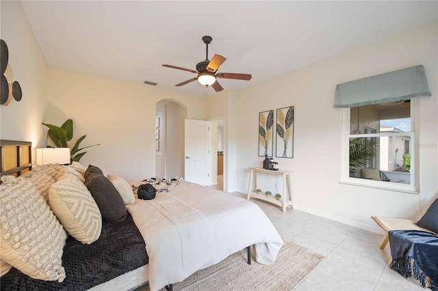 bedroom with arched walkways, ceiling fan, light tile patterned floors, visible vents, and baseboards