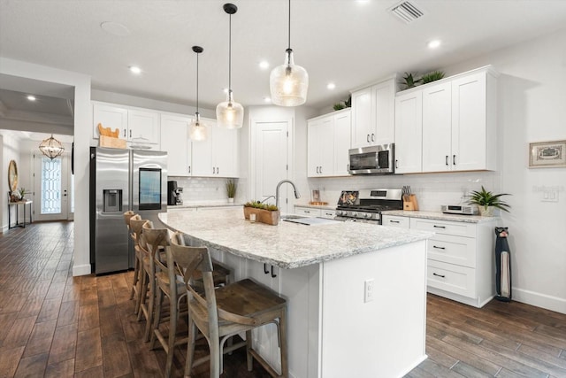 kitchen featuring pendant lighting, a center island with sink, decorative backsplash, white cabinetry, and stainless steel appliances