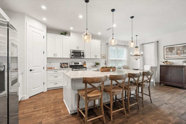 kitchen with white cabinetry, an island with sink, appliances with stainless steel finishes, dark wood-type flooring, and hanging light fixtures