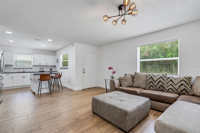 living room featuring a textured ceiling, light hardwood / wood-style flooring, a chandelier, and sink