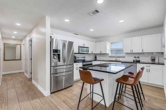 kitchen featuring white cabinets, stainless steel appliances, light hardwood / wood-style floors, a breakfast bar area, and a kitchen island