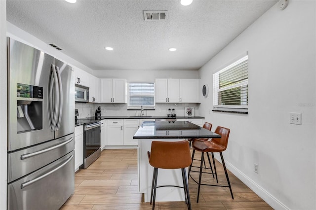 kitchen featuring white cabinetry, a kitchen island, stainless steel appliances, and light hardwood / wood-style floors