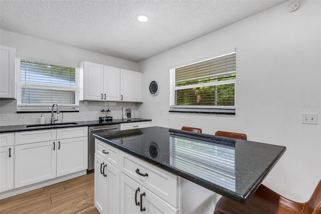 kitchen with a center island, sink, white cabinetry, light wood-type flooring, and dark stone counters