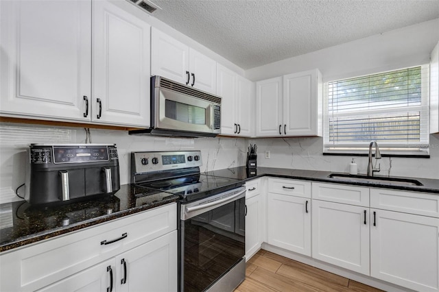 kitchen featuring a textured ceiling, appliances with stainless steel finishes, light hardwood / wood-style floors, sink, and white cabinets