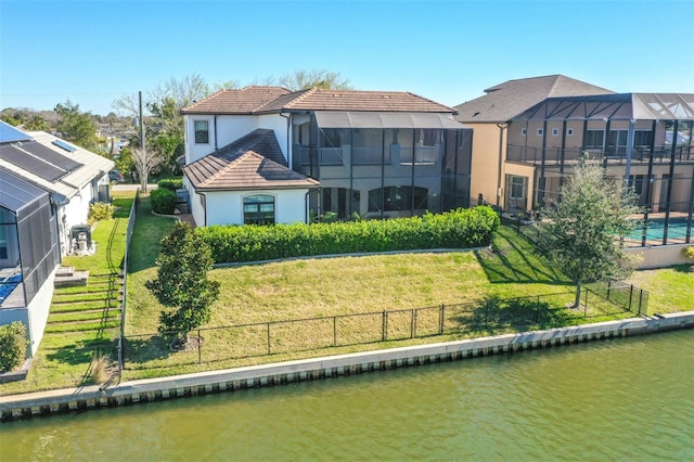 rear view of house with a water view, a lawn, and a lanai