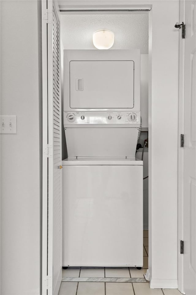 clothes washing area featuring stacked washer and dryer, light tile patterned flooring, and a textured ceiling