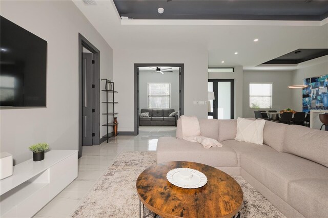 living room featuring ceiling fan, a wealth of natural light, and a raised ceiling