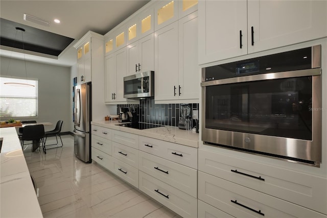 kitchen featuring white cabinets, light stone countertops, stainless steel appliances, and decorative backsplash