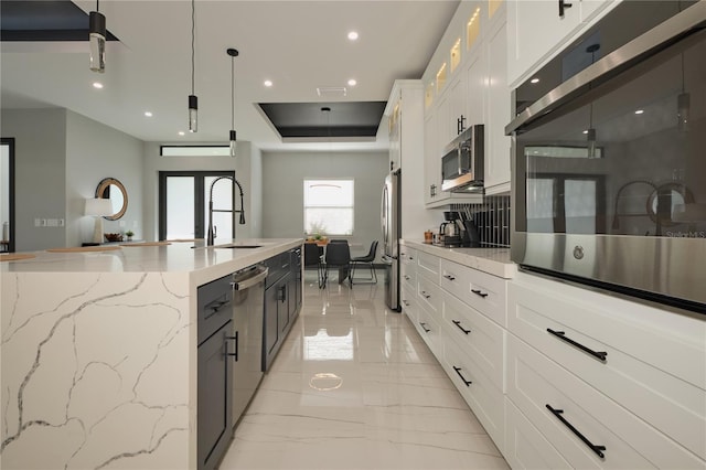 kitchen featuring pendant lighting, appliances with stainless steel finishes, sink, light stone counters, and white cabinets