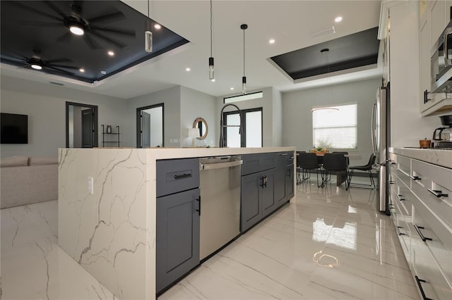 kitchen featuring a center island with sink, ceiling fan, stainless steel appliances, and a tray ceiling