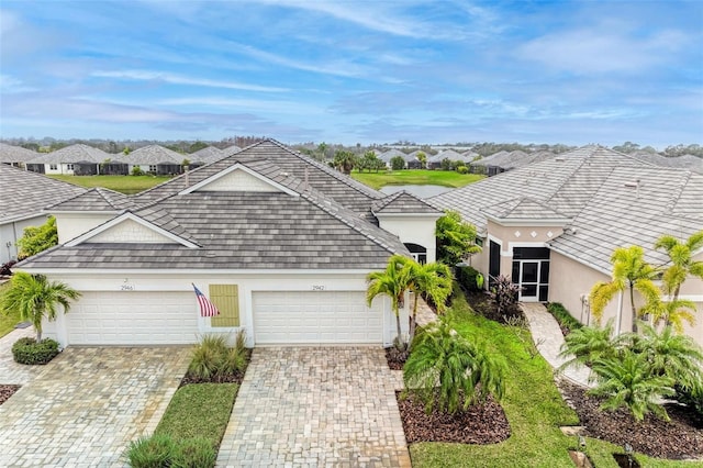 ranch-style home with decorative driveway, an attached garage, a residential view, and stucco siding