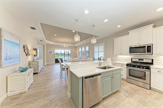 kitchen with a raised ceiling, light countertops, backsplash, appliances with stainless steel finishes, and a sink