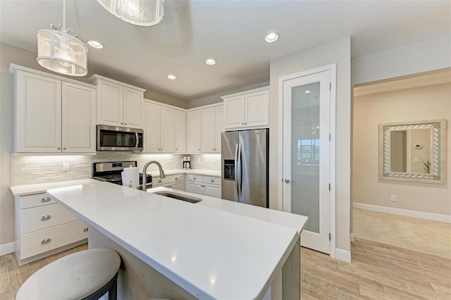 kitchen featuring a sink, light countertops, appliances with stainless steel finishes, backsplash, and light wood finished floors