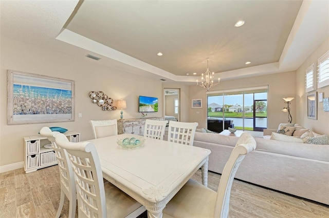 dining area featuring recessed lighting, a raised ceiling, light wood-style flooring, and an inviting chandelier