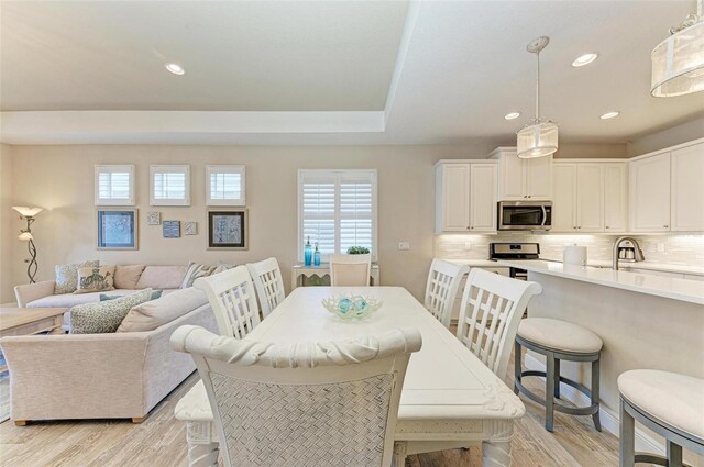 dining space with a tray ceiling, light wood-style flooring, and recessed lighting