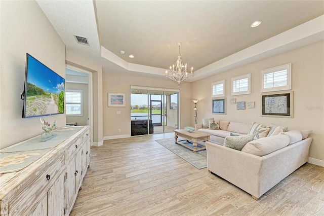 living room with a healthy amount of sunlight, light wood-style flooring, visible vents, and a tray ceiling