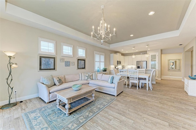 living room with light wood-style floors, recessed lighting, a raised ceiling, and baseboards