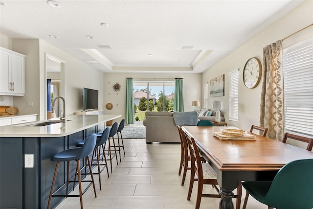 tiled dining area featuring a raised ceiling and sink