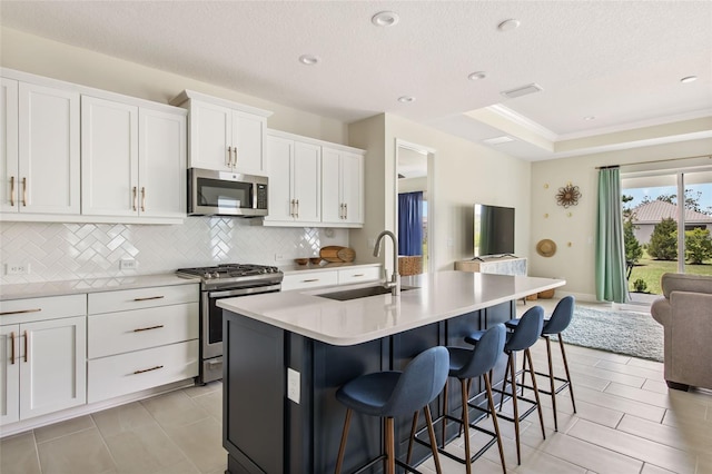 kitchen with a kitchen breakfast bar, an island with sink, stainless steel appliances, sink, and white cabinetry